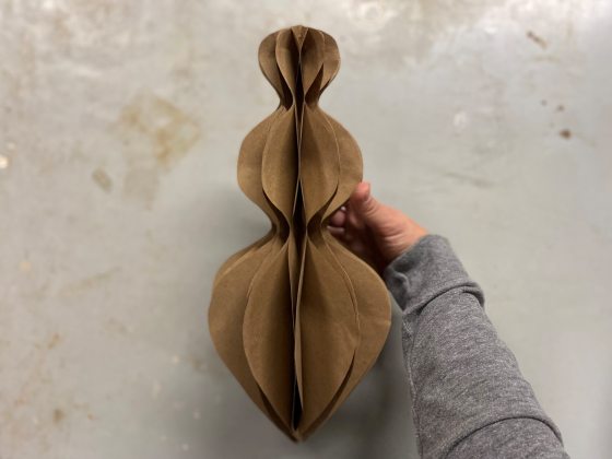 A person holding a brown paper ornament ready to be decorated.